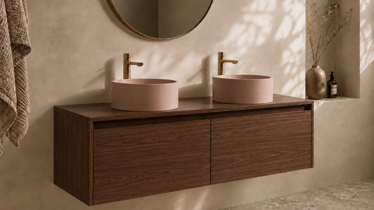 A floating double-sink bathroom vanity with a walnut cabinet, two round blush pink vessel sinks, and gold faucets, set against a textured beige plaster wall. 1200 wide vanity 